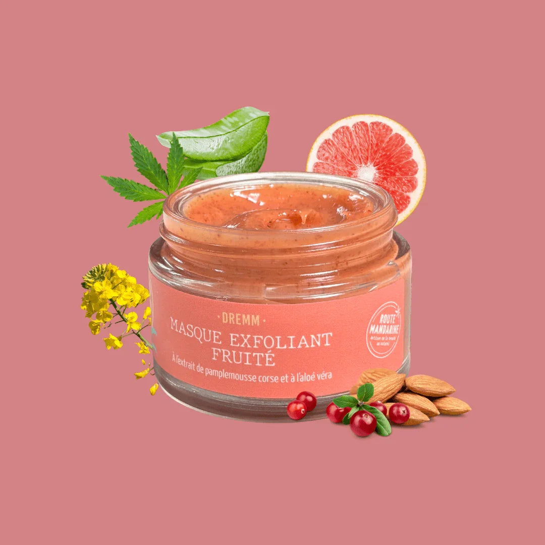 gommage visage nourrissant et fruité DREMM en pot en verre ouvert, entouré des ses ingrédients : pamplemousse, aloe vera, amandes et baies sur fond rose.