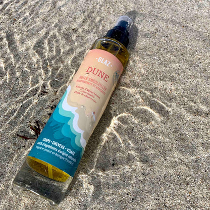 Huile sèche dune pour le corps et les cheveux sur le sable avec la mer